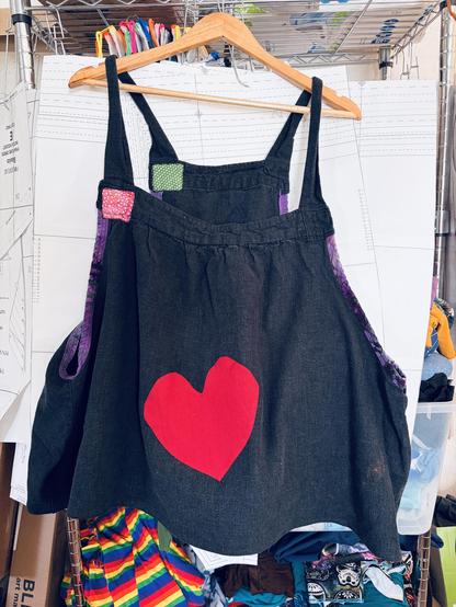 A black linen pinafore top, with a big red heart in the middle, and some small square patches on the shoulder.
