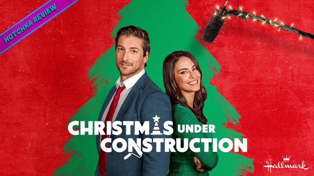 Hotchka Review: Christmas Under Construction. A man in a suit and a woman in a green sweater smile confidently with arms crossed in front of a stylized Christmas tree on a red background; text reads "Christmas Under Construction." The Hallmark logo is in white at the bottom right corner.