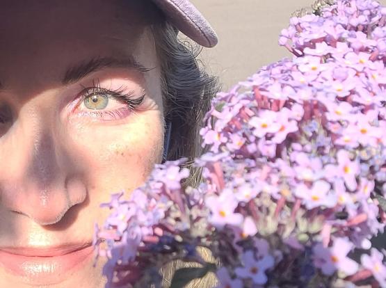 Me next to some buddleia smiling I have purple eyeshadow that matches it and very green eyes