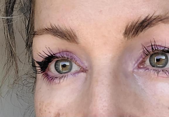 Close up of a purple eye shadow with a French clock at the tail with mascara and fluffy eyebrows. I have green and orange eyes.