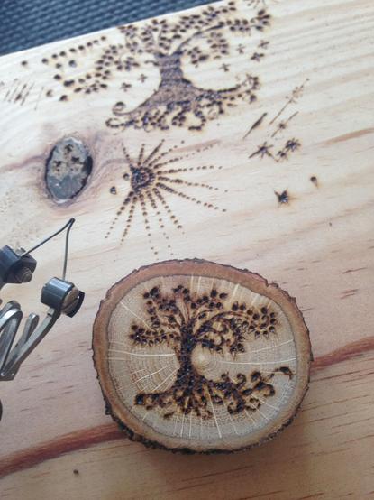 Some pyrography (wood burning) doodles on a plank of wood with tree and some patterns. Also a small wood round made of a slice of oak tree with a drawing using pyrography on it of a tree with roots beneath.