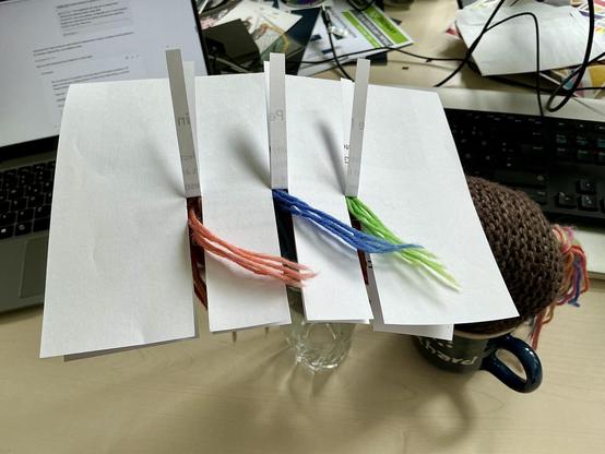 Max, das bunte Strickhorn, hat sich hinter einem Blatt Papier versteckt; durch drei reingeschnittene Spalte ragen jeweils ein paar seiner regenbogenbunten Mähne durch, sodass nur "drei Farben" für den heutigen Fotovorschlag sichtbar sind: rosa, blau und grün.