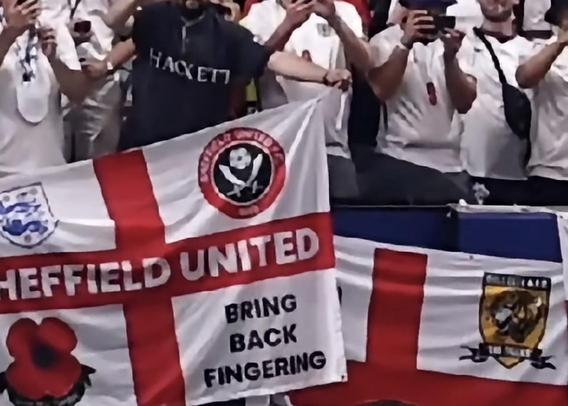 Screenshot of the England fans from England v Mexico in the World Cup. It’s an imagine of fans holding an England Flag with a poppy, a Sheffield United club badge, the England football team badge and the phrase “bring back fingering”