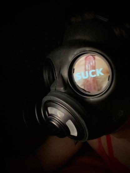 Rina in the dark, wearing a gas mask with an image showing a cock with the caption "suck" reflected in the lens