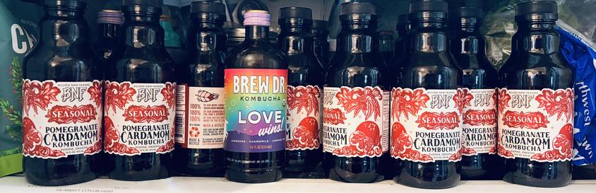 A row of kombucha bottles on the bottom shelf of a fridge.