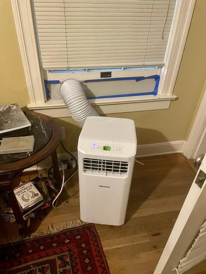 A portable air conditioner with its vent very temporary stuffed into the bottom half of a wood sash window.