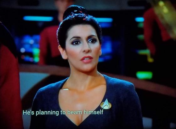 Star Trek The Next Generation scene. We're on the bridge of the Enterprise. Various crewfolk are crewfolkin' in the background and we see Counselor Troi standing and looking like she's half offended and half interested in something. Closed caption reads, "He's planning to beam himself"