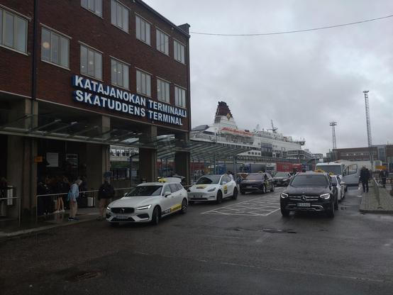 Blick auf einen Taxihaltplatz am Katajanokan Terminaali wie es an einem Gebäude steht. Im Hintergrund die Viking Cinderella am Anleger.