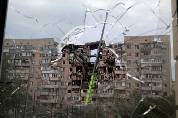 A multistorey residential building left partially destroyed by a Russian missile strike on the Ukrainian capital is seen through a broken window.