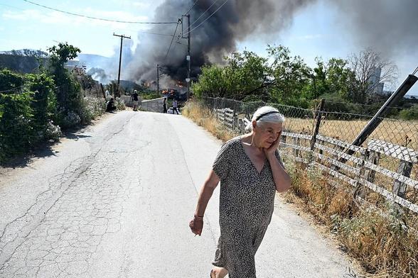 A white-haired woman walks away from a fire in disbelief.