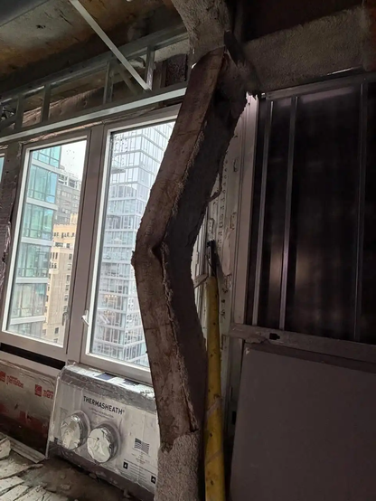 A photo inside a building showing an old steel beam buckling in front of a window indicating it it many stories up.