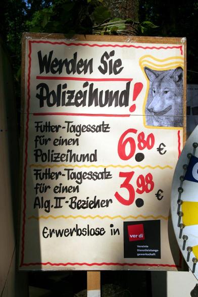 Foto im Hochformat. Ein Plakat, das einen grauen Hundekopf zeigt, daneben der Text „Werden Sie Polizeihund! Futter-Tagessatz für einen Polizeihund: 6,80 € – Futter-Tagessatz für einen Alg-II-Bezieher: 3,98 € – Erwerbslose in ver.di“