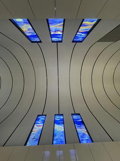 Abstract ceiling with curved panels and six glowing blue art light panels.