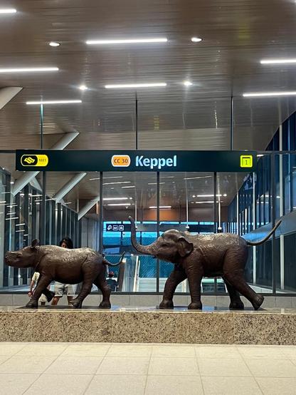Elephant and rhinoceros sculptures in front of a Keppel MRT station sign.