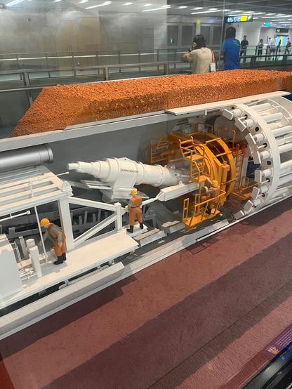 Cutaway display of a tunnel boring machine with miniature workers and machinery inside an underground transit exhibit.