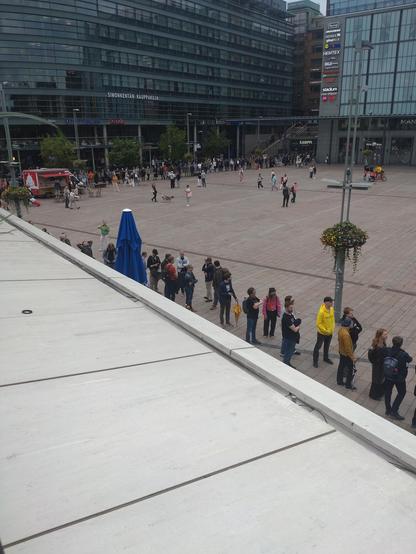 Eine Schlange wartender Leute verläuft über einen belebten Platz im Zentrum von Helsinki.