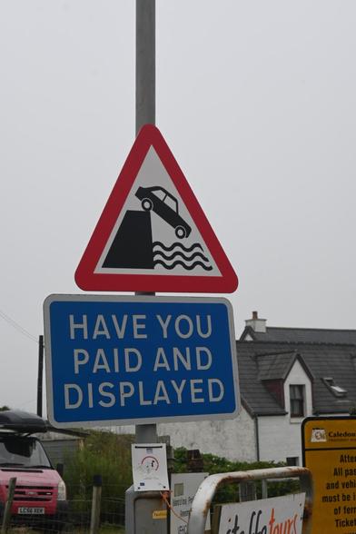 two traffic signs on one post. Above a red rimmed triangle with a car falling off a pier into water. Underneath a blue rectangular sign with these words in white: "Have you paid and displayed"