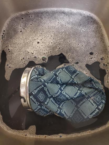 A Royal Model 501 hand vacuum's cloth bag sits in a sink of water that appears nearly black in color.