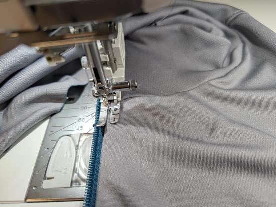 A zipper being sewn into a shirt. The foot on the sewing machine has no zipper notches and is just a fancy straight stitch foot.