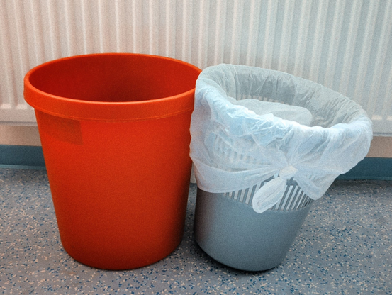 Ein roter und ein grauer Mülleimer vor einem Heizkörper