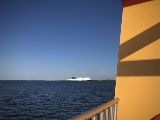 Neben gelborange Schiffsaufbauten im Vordergrund rechts ist  etwas entfernt ein größeres Schiff.
