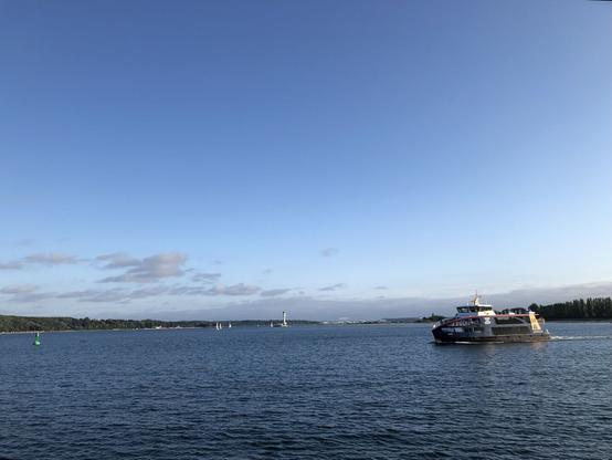Blickrichtung Kiel, eine kleine Förde-Fähre kreuzt. Dünne Wolken am Himmel.