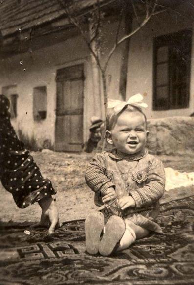 A vintage photograph of a smiling baby seated on an ornate rug outdoors