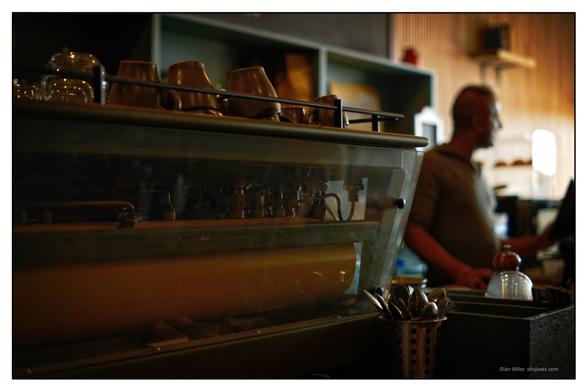 Colour photo of retro cafe espresso machine with barista in the background.