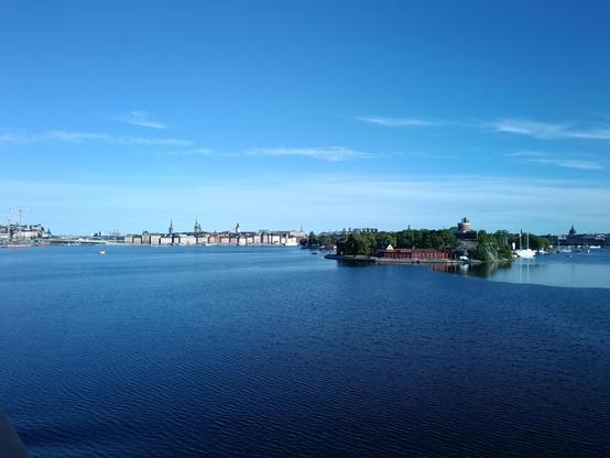 Blick vom Schiff auf die Altstadt in Stockholm. Der Himmel ist hellblau, das Wasser kräftig dunkelblau.