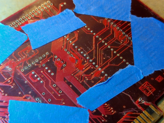 blue tape holding a nearly invisible piece of plastic on top of the board that has been painted red in a couple of spots.