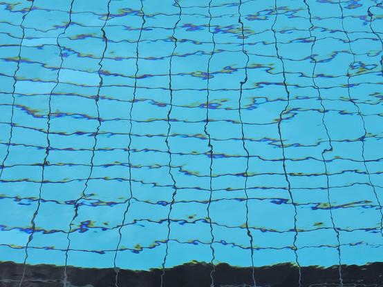 Close-up of bright blue swimming pool water with wavy reflections over a tiled grid pattern.