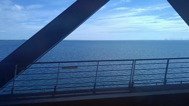 Blick aus dem Zugfenster auf den Öresund. Am Zugfenster ziehen die schrägen Stahlstützen der Brückenkonstruktion vorbei. Dahinter liegt die tiefblaue Ostsee und ein blauer Himmel mit Schönwetterwolken.