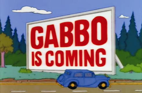 Bild aus der Zeichentrickserie Die Simpsons. Eine große Reklametafel mit der Aufschrift „Gabbo is coming“, also „Gabbo kommt“.
