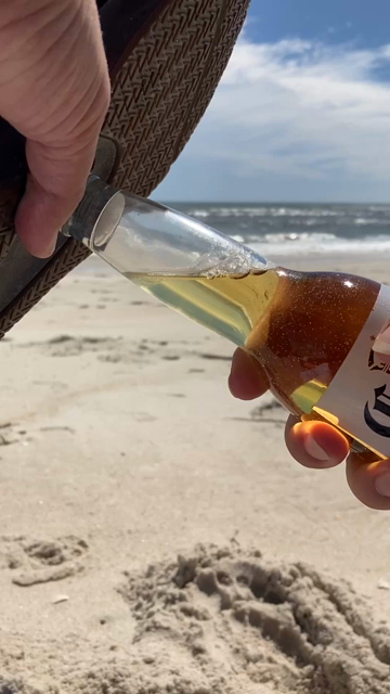 A 4 second video of your narrator opening a bottle of Corona with the sole of a sandal that has a bottle opener built in. In the background are a sandy beach, and then the blue ocean with white wave caps.