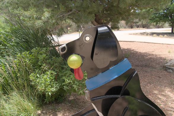 Metal sculpture of a dog with a tennis ball in its moth