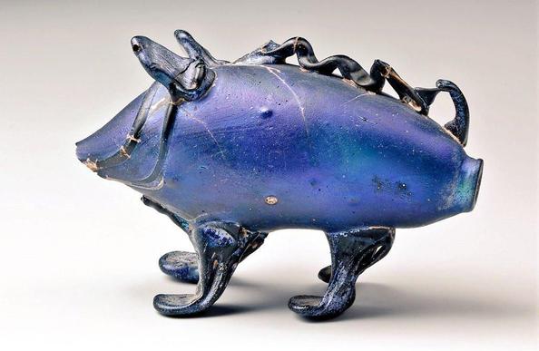 Deep blue glass vessel shaped like a stylized animal with four legs, a pointed snout, and decorative ridges along its back, resembling a whimsical pig.
