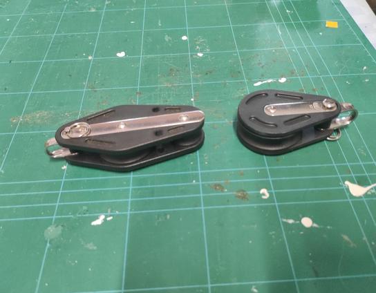 Small plastic tackle block and pulley on a green cutting mat.
