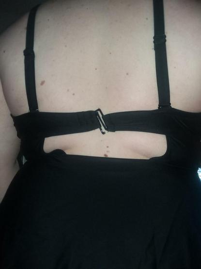 A closeup of a pale woman's back. She's wearing a black one-piece swimsuit. The back of the chest band is held closed by a plastic clip, which is warped under the strain of the tight suit.