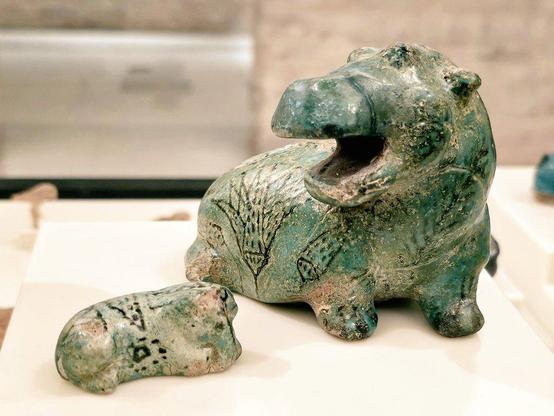 Two turquoise-blue hippopotamus figurines, one larger with black plant motifs and an open mouth, the smaller one lying on its side.