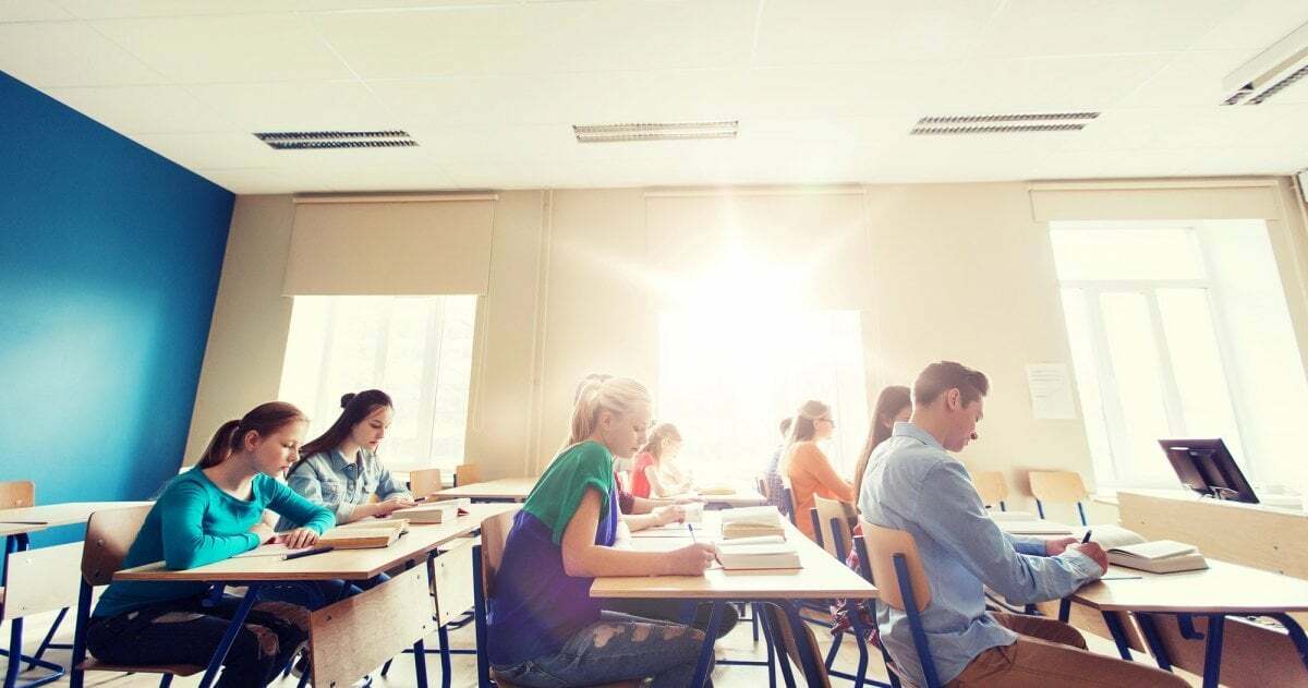 Mehrere Schüler:innen sitzen in einem Klassenraum, durchs Fenster scheint hell die Sonne