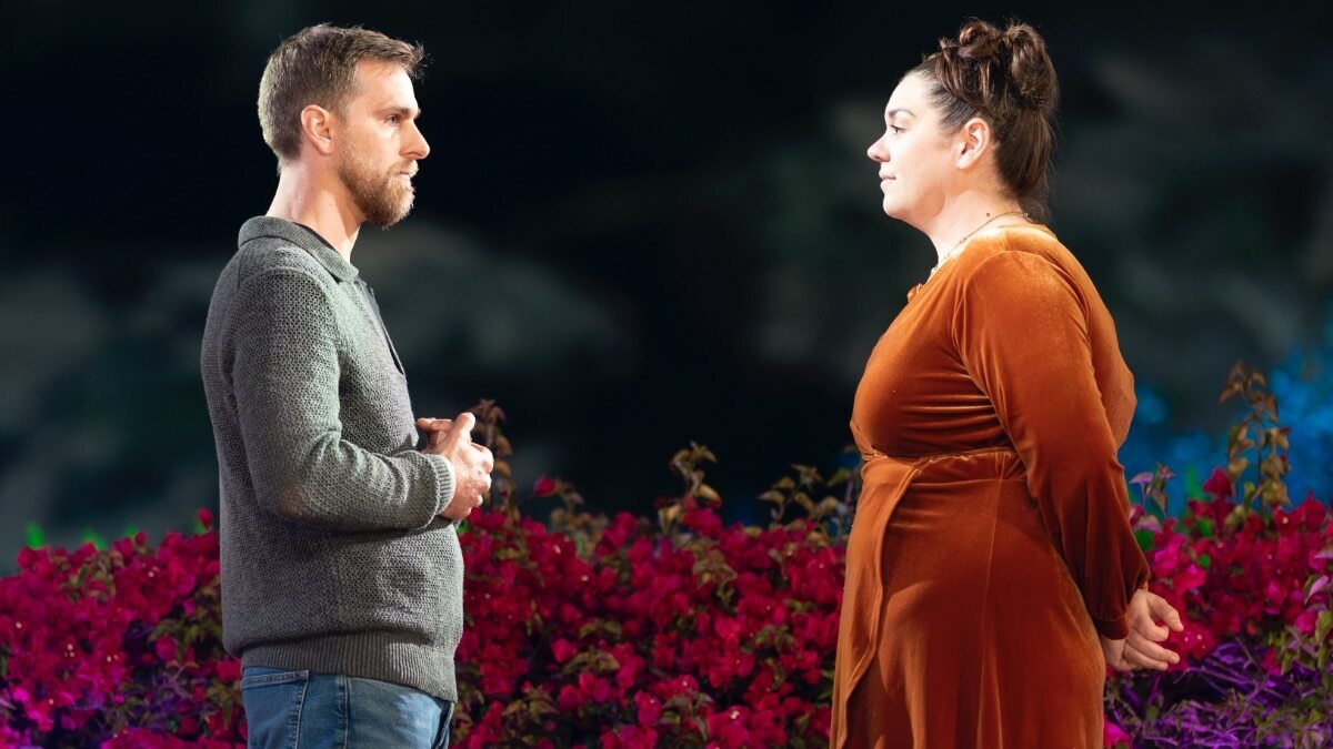 Two people stand in front of rose bushes outside at night and look at each other