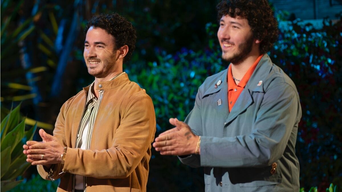 Two people standing outside at night, facing the same direction, clapping and smiling