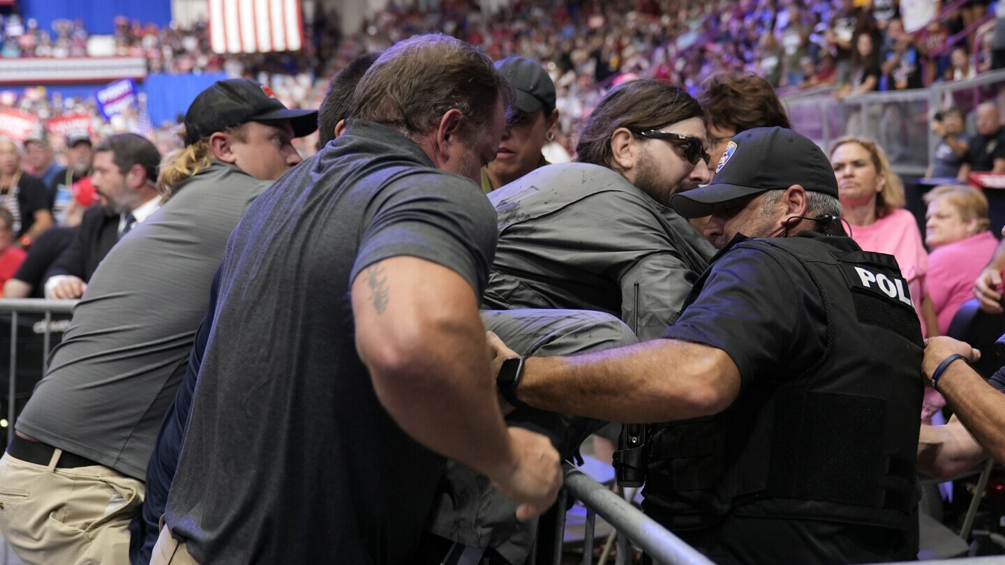 Police remove a man, center with sunglasses, who had climbed onto the media riser, as Republican presidential nominee former President Donald Trump speaks at a campaign event, Friday, Aug. 30, 2024, in Johnstown, Pa. (AP Photo/Alex Brandon) Police remove a man, center with sunglasses, who had climbed onto the media riser, as Republican presidential nominee former President Donald Trump speaks at a campaign event, Friday, Aug. 30, 2024, in Johnstown, Pa. (AP Photo/Alex Brandon)