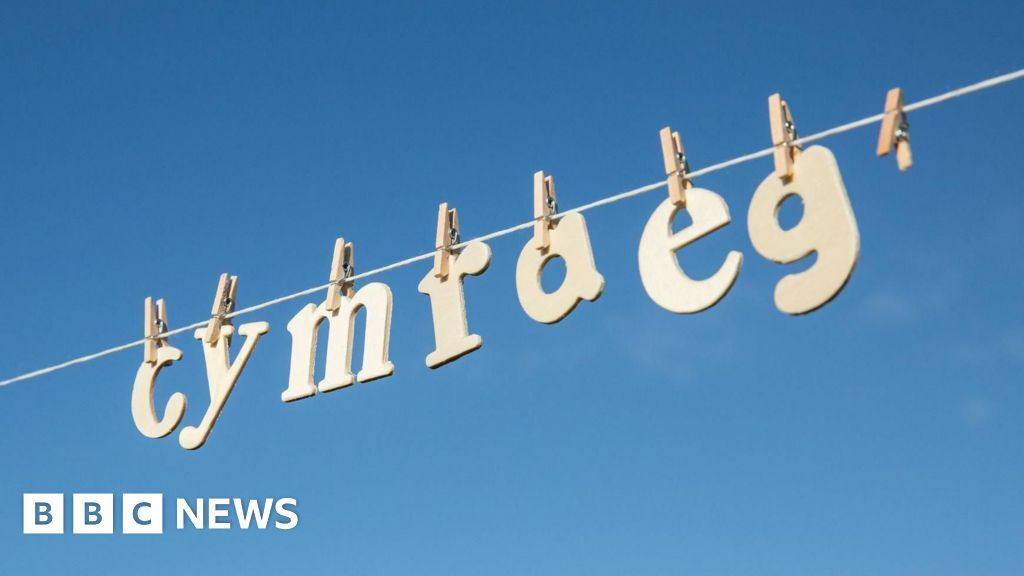 wooden letters hung on a clothes line in front of a clear blue sky, spelling out cymraeg, or welsh in English