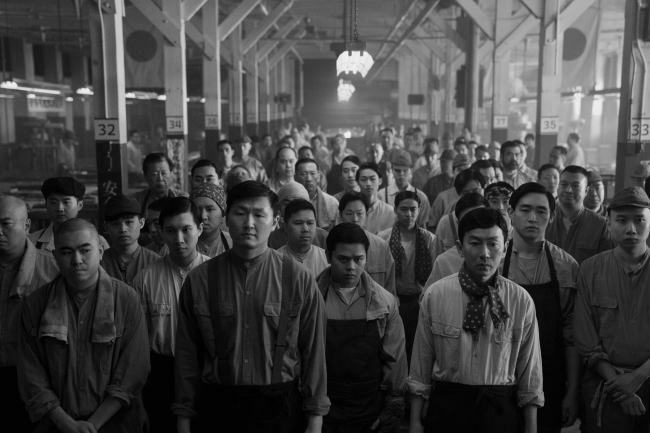 A black and white image of men lined up in a factory hall from Episode 5 of Season 2 of 'Pachinko'