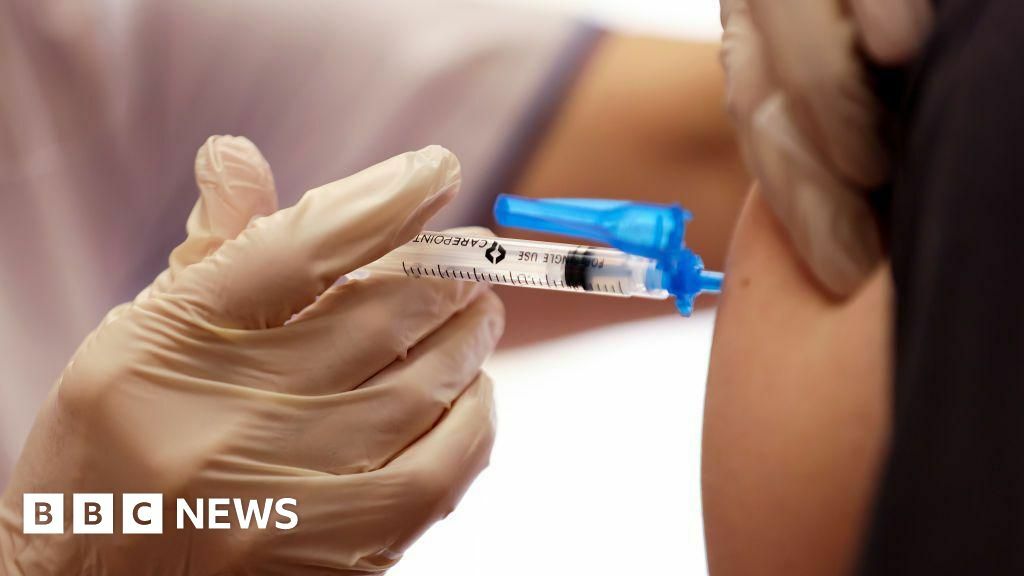 A close-up photo of a gloved hand injecting a vaccine into a person's arm.