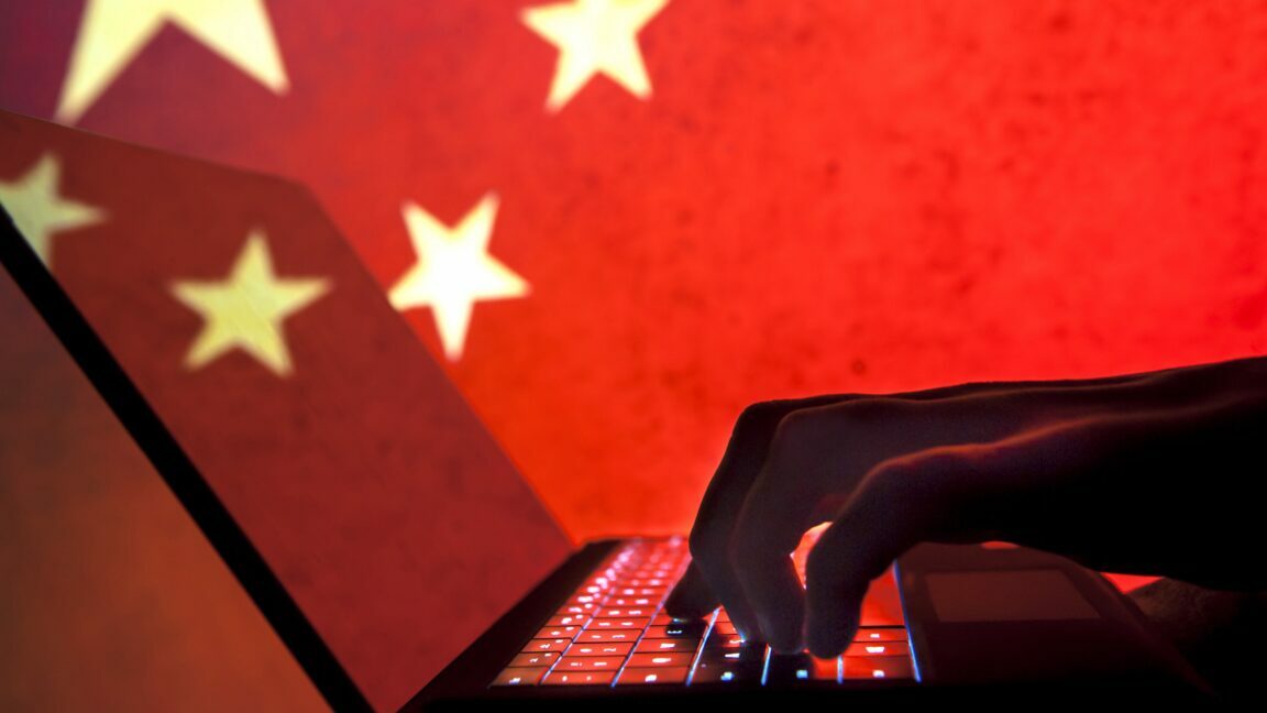 A person typing on a laptop with a Chinese flag in the background