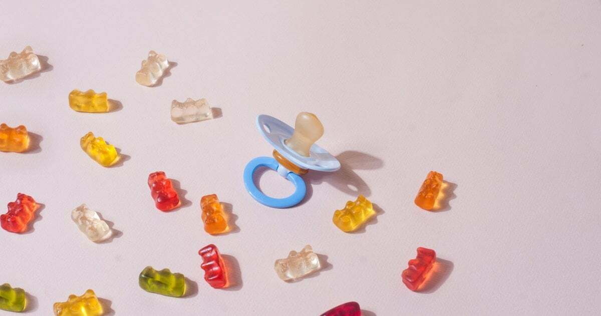 Draufsicht: Gummibärchen und ein Schnuller liegen auf einem altrosafarbenen Hintergrund.