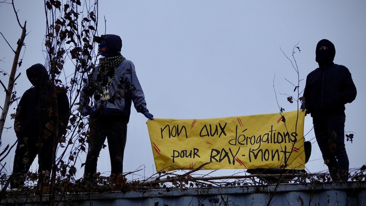 Trois personnes masquées portent une banderole sur laquelle il est écrit : « non aux dérogations pour Ray-Mont ».