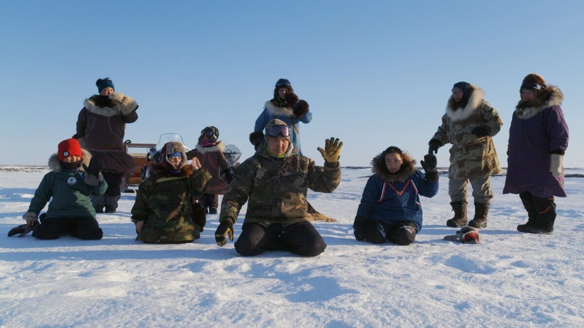 A group of people in winter clothes on an icy snowdrift, holding their hands up and singing